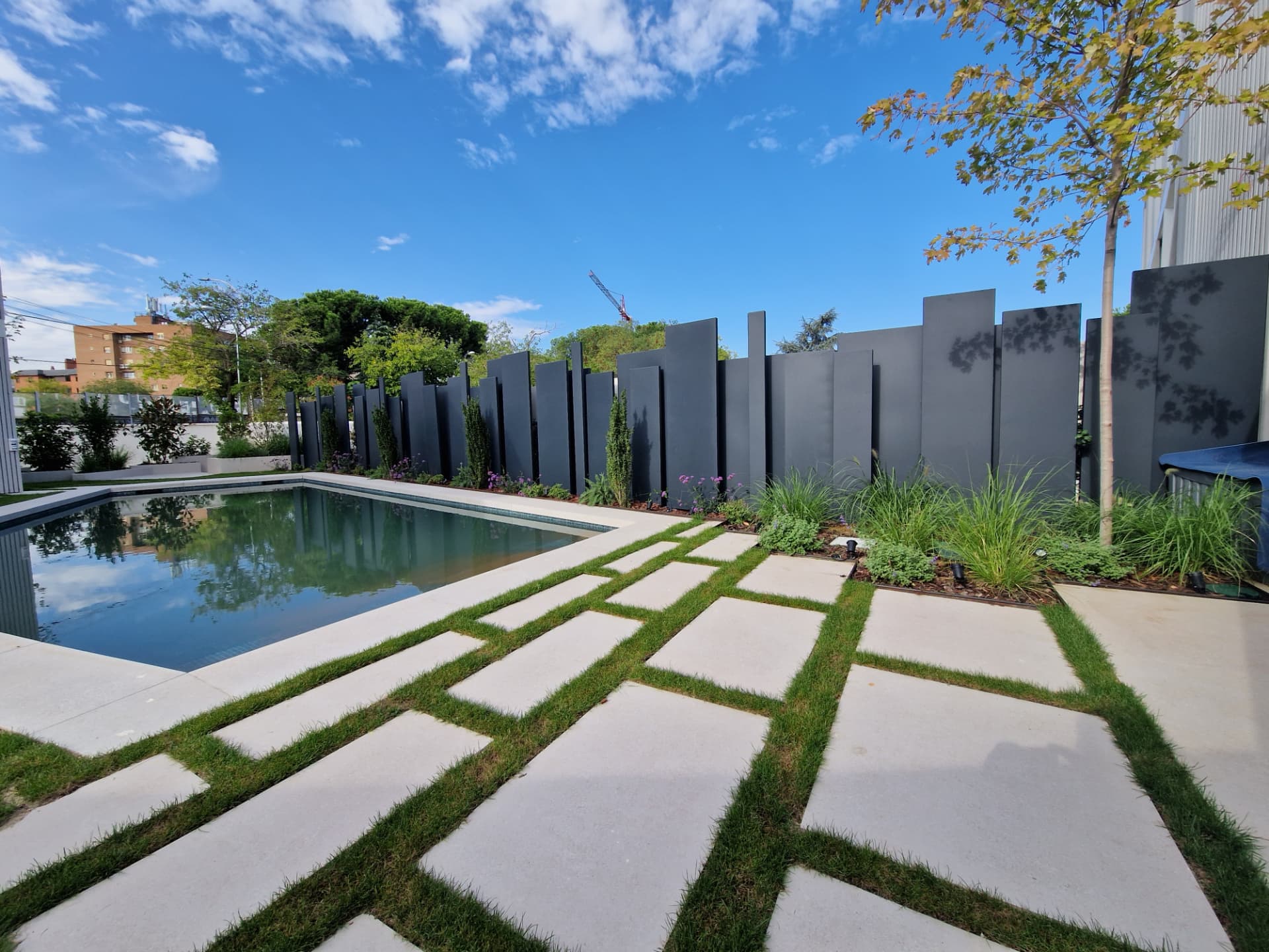 Residential swimming pool with geometric stone paving, ornamental grasses and sculptural privacy screens