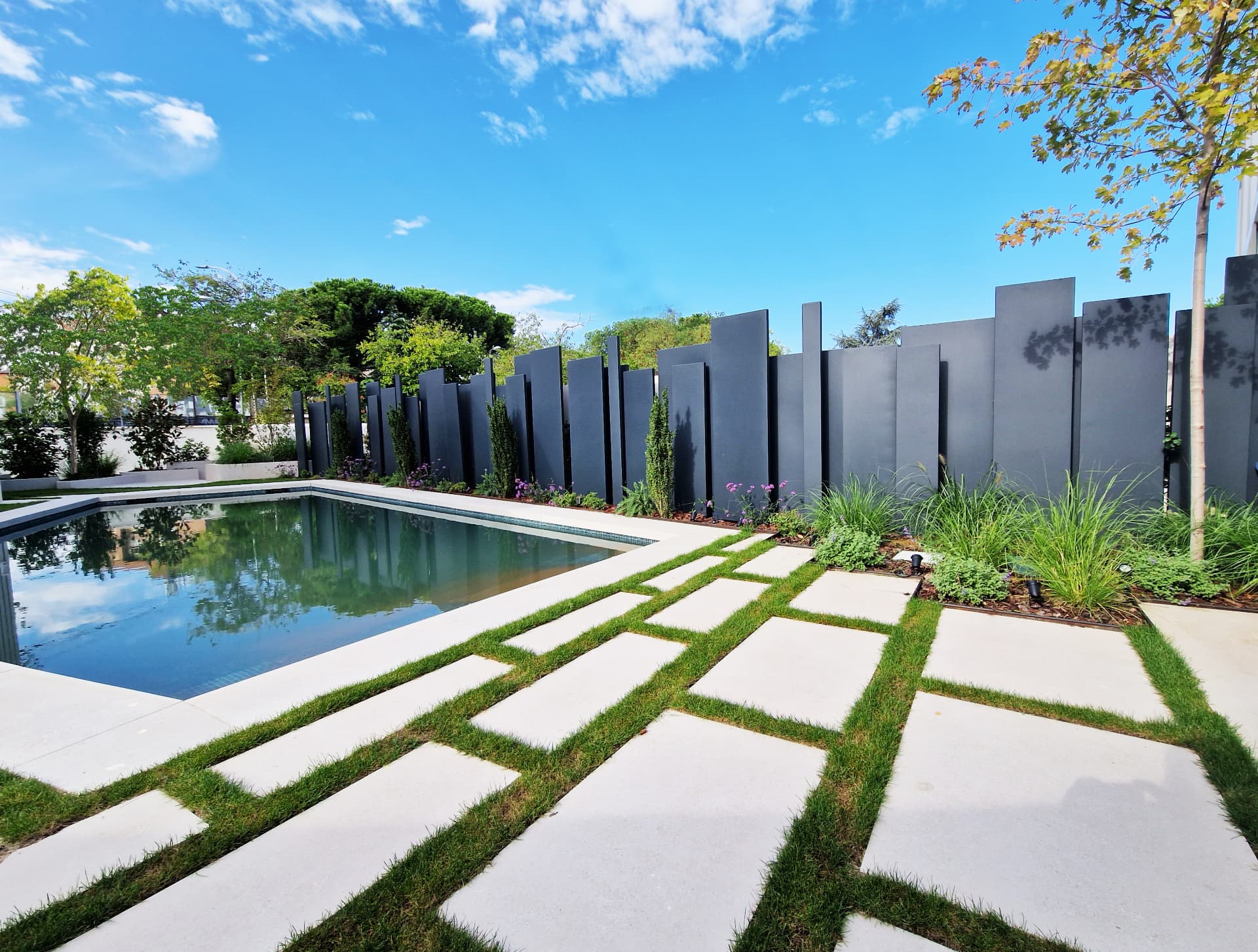 Swimming pool bordered by grass-jointed paving, ornamental grasses and tall dark privacy panels